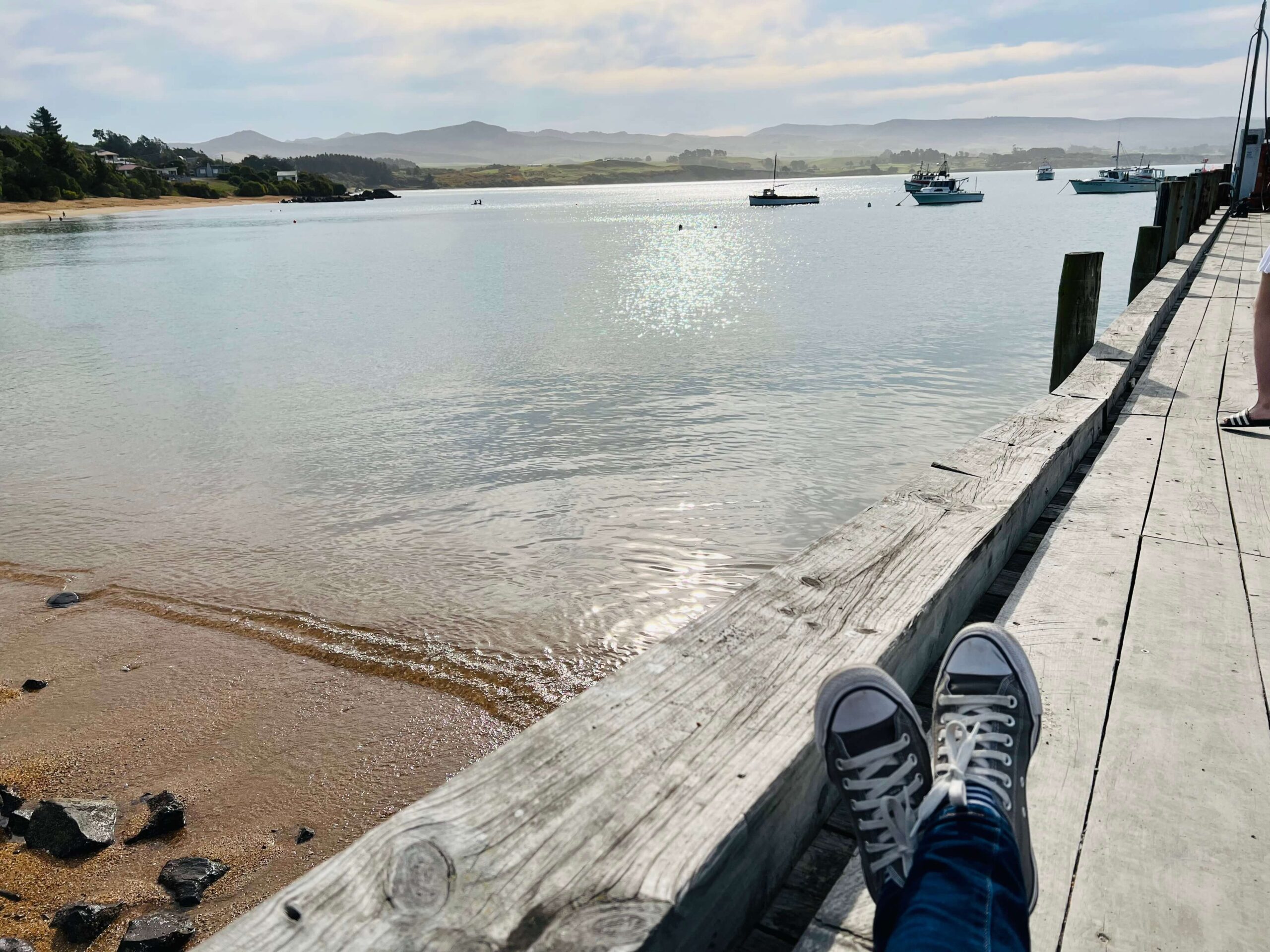 Woman's legs sitting on a wharf with the ocean in the distance