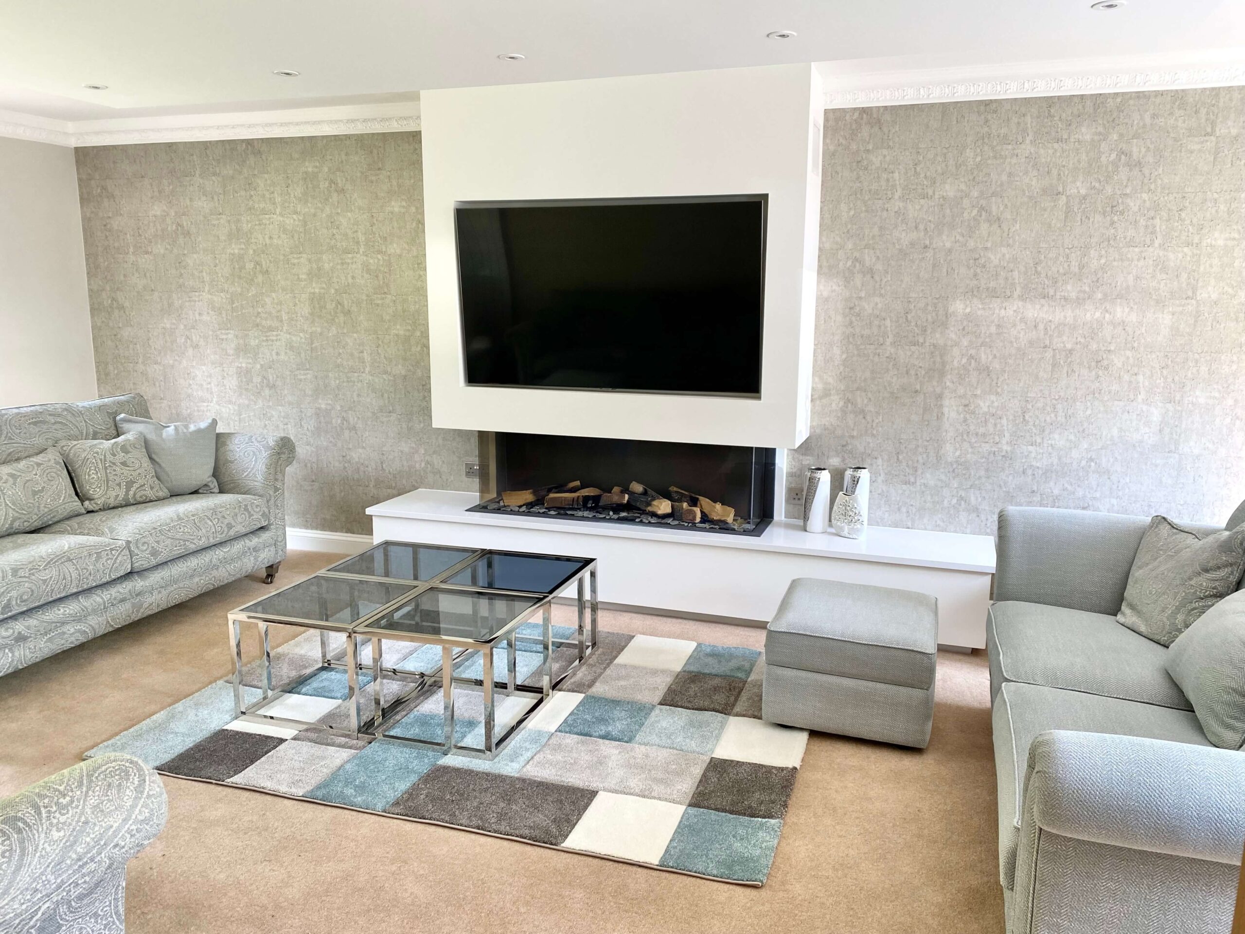 A neutral toned sitting room with sofas, a TV, and a glass table 