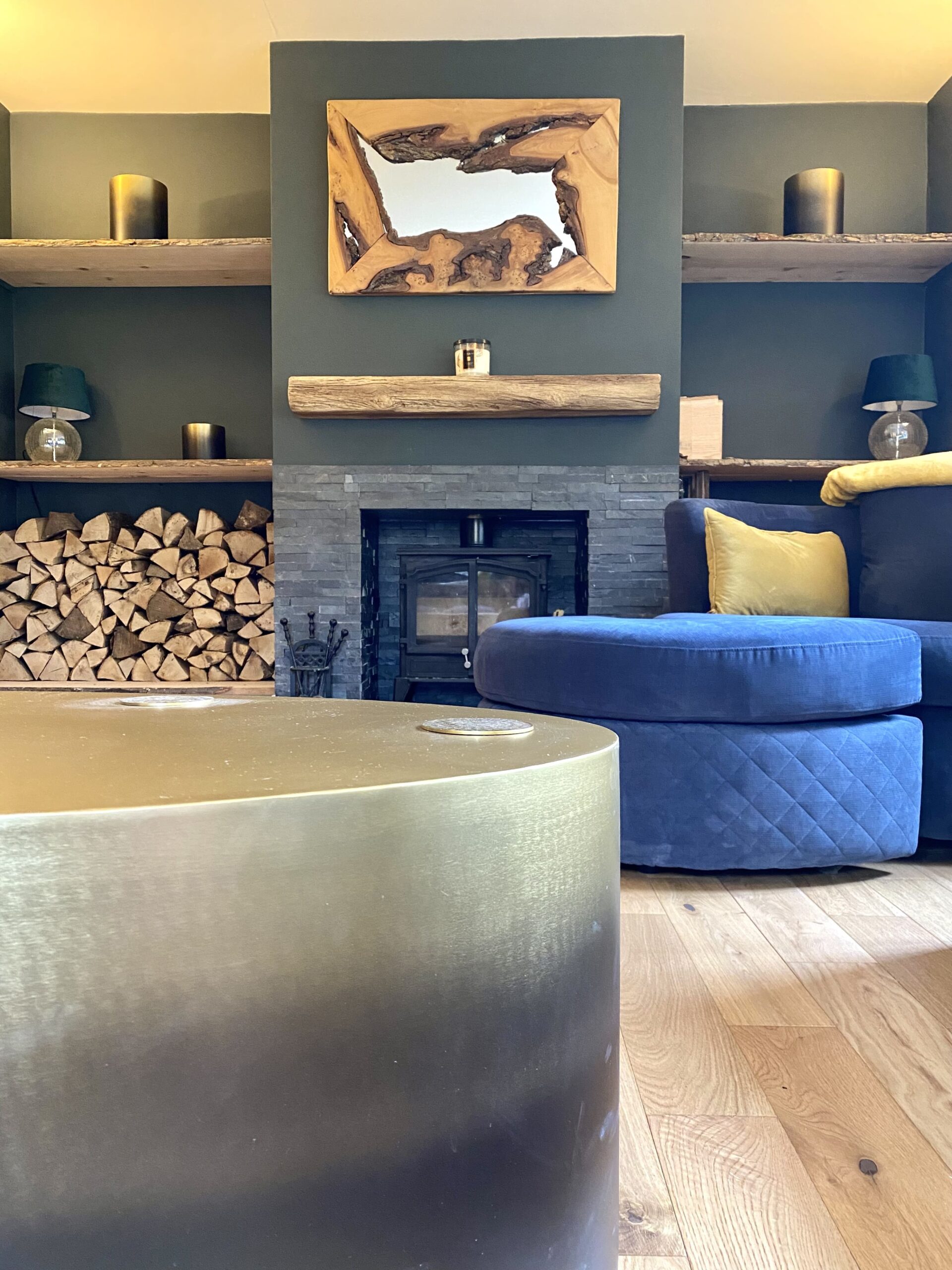 A table and ottoman in a blue toned room in front of a fireplace and art 